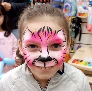 Smiling child with a pink and black tiger face painting design